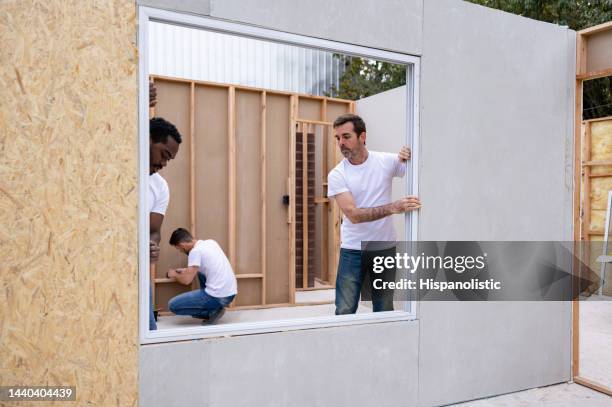 volunteers installing a window while building a house - habitat for humanity stock pictures, royalty-free photos & images