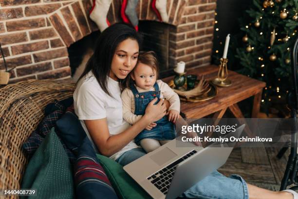 online christmas party. happy black mom and daughter using laptop making video call celebrating xmas distantly sitting on floor at home, waving hands. new year and winter holidays celebration concept - hawaii christmas stockfoto's en -beelden