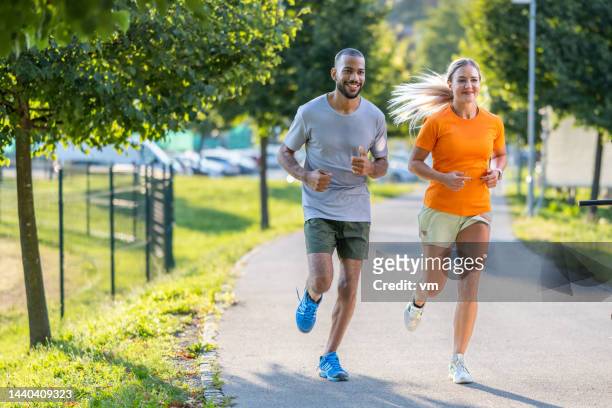 smiling young couple jogging in city park together - wide shot stock pictures, royalty-free photos & images