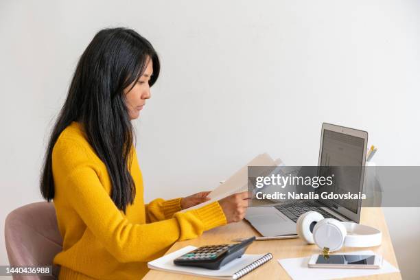 asian woman working at home looking at documents. beautiful japanese female freelancer. overworking, filling out papers, documents and reports - steuerberater stock-fotos und bilder