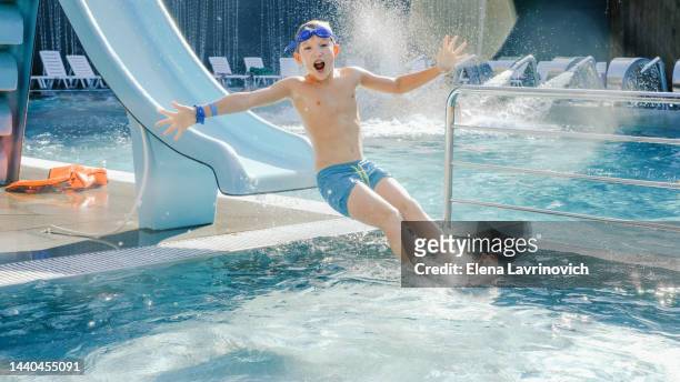 happy 10 year old boy is rolling down the slide into the pool. entertainment in the water park - indoor kids play area stock-fotos und bilder