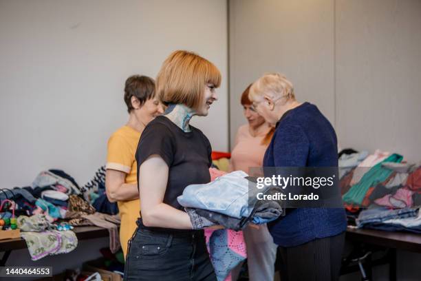 eine generationenübergreifende gruppe von flüchtlingen sucht kleidung in einem spendenzentrum - philanthrop stock-fotos und bilder
