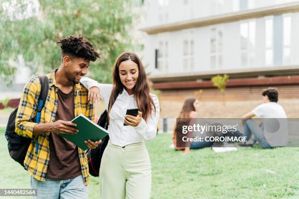 college student couple walking out of class while having fun looking at mobile phone. - campus universidad fotografías e imágenes de stock