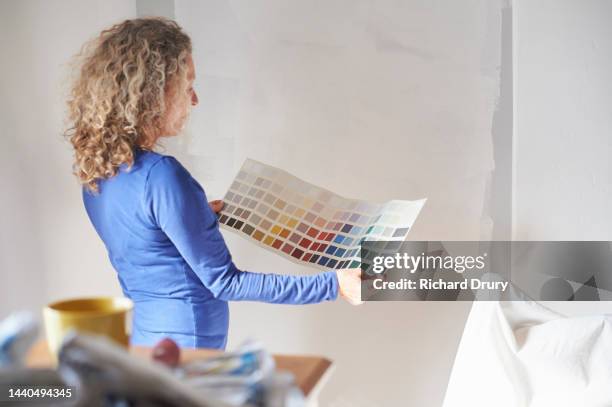a mature woman studying a paint colour swatch - decorating stock pictures, royalty-free photos & images