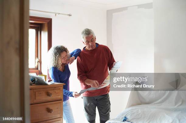 a mature couple looking at a paint colour chart - decorator stock pictures, royalty-free photos & images