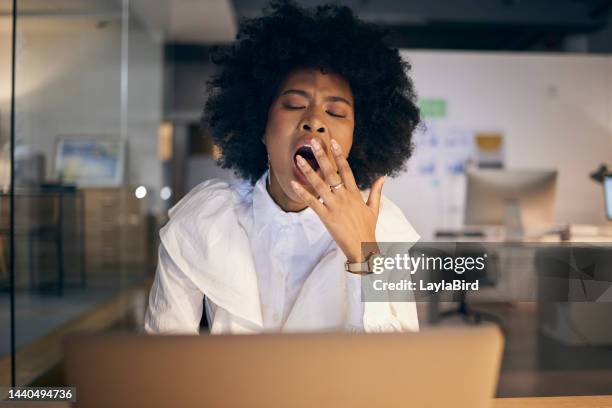 tired, burnout and business woman yawning with a laptop at night in a dark office. stress, fatigue and african corporate worker reading a proposal on the internet with a yawn during overtime - gapen stockfoto's en -beelden