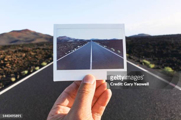 Man holding an instant photo in front of a road in a volcanic landscape