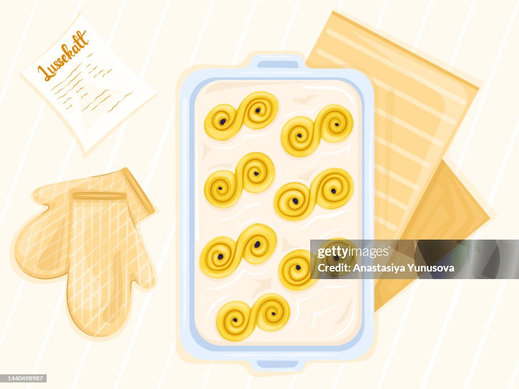 Home baked saffron buns on oven-tray with recipe and pot holders on table
