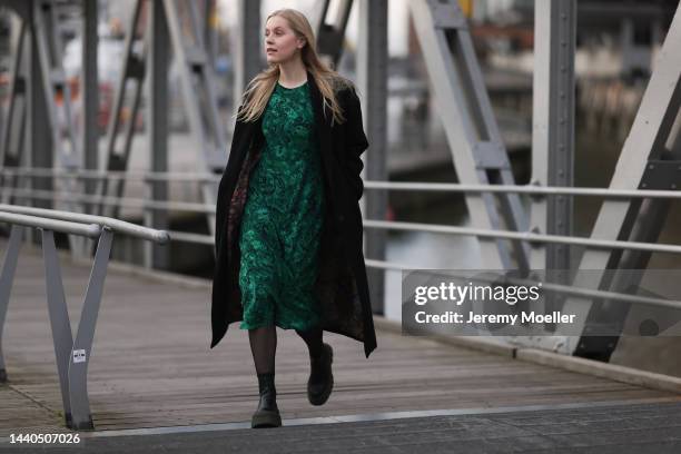 Lil Paulin seen wearing a green patterned long dress, a black long coat and black and dark green leather boots by Copenhagen Studios on November 08,...