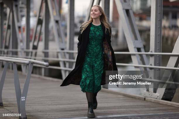 Lil Paulin seen wearing a green patterned long dress, a black long coat and black and dark green leather boots by Copenhagen Studios on November 08,...