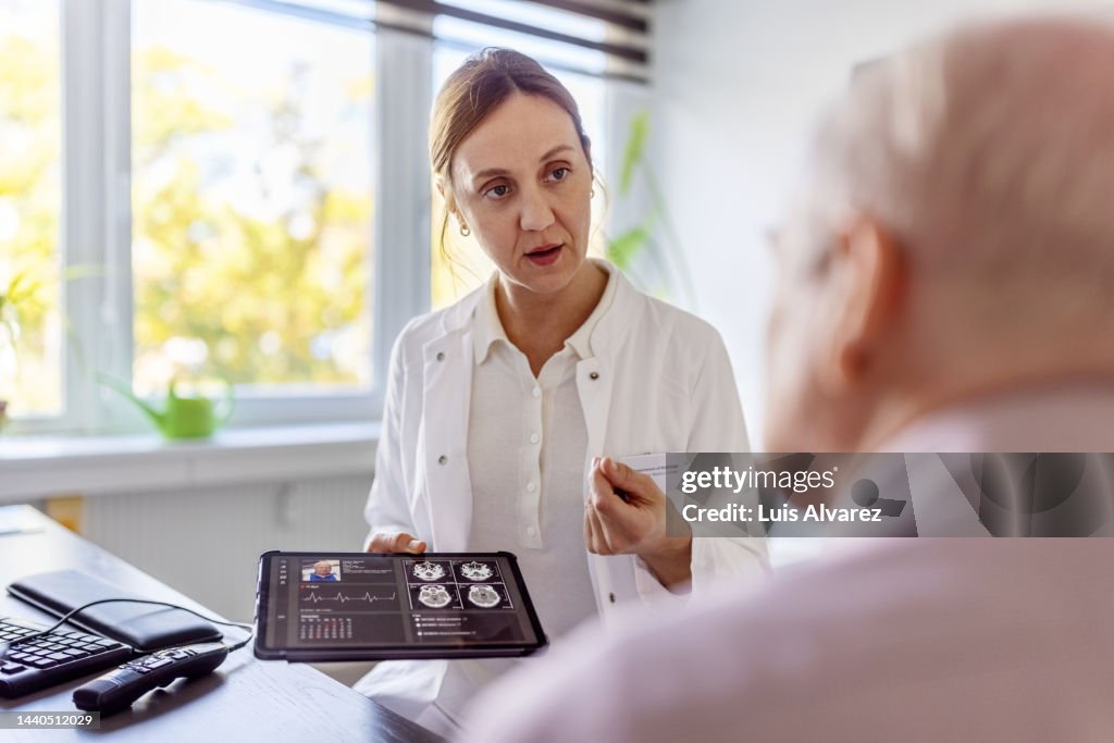 Doctor using a digital tablet to discuss a brain scan with a senior patient in clinic