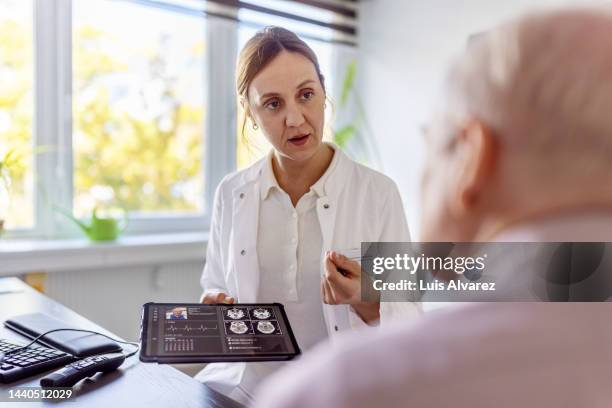 doctor using a digital tablet to discuss a brain scan with a senior patient in clinic - person screened for cancer stock pictures, royalty-free photos & images
