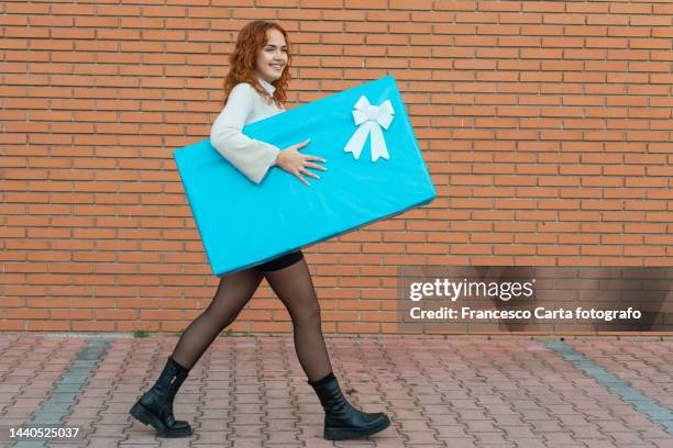 young woman carrying a big light blue gift box - giant woman photos et images de collection