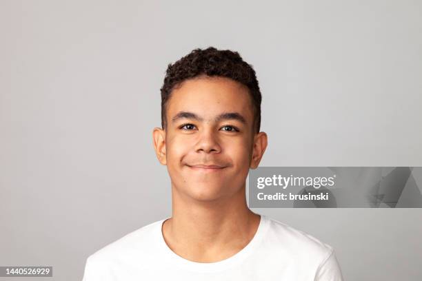 close-up studio portrait of a cheerful 13 year old teenager boy in a white t-shirt against a gray background - 13 stockfoto's en -beelden