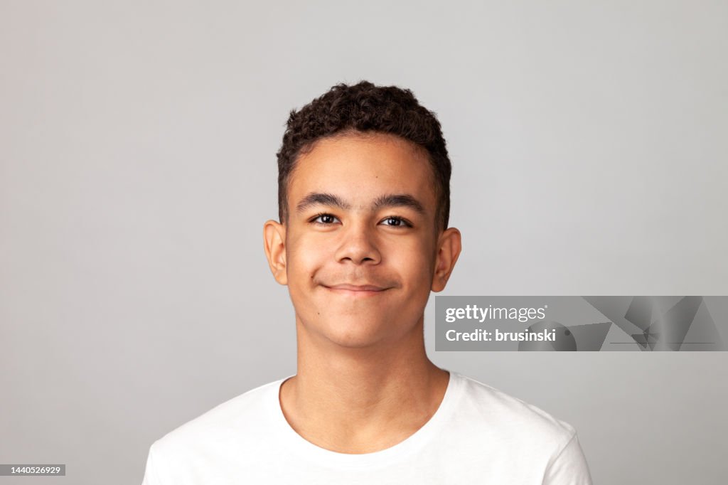 Close-up studio portrait of a cheerful 13 year old teenager boy in a white t-shirt against a gray background