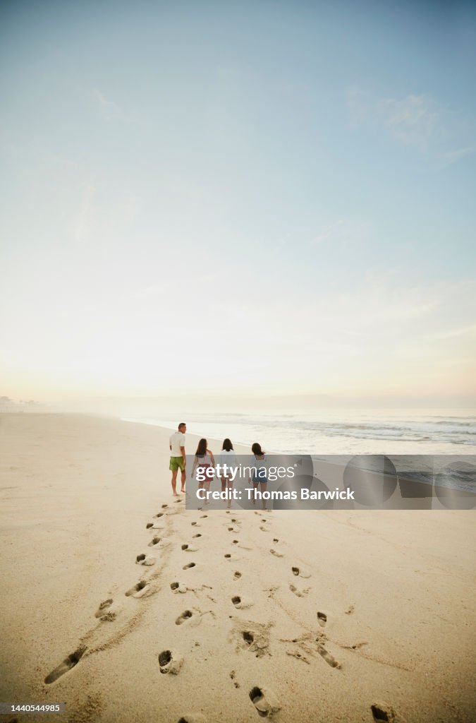 Wide shot of family walking on empty tropical beach at sunrise