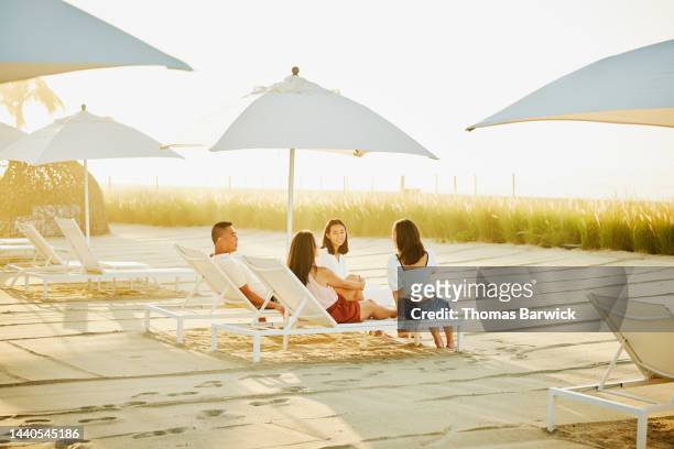 wide shot of smiling family relaxing in lounge chairs at beach resort - baja california sur stock pictures, royalty-free photos & images