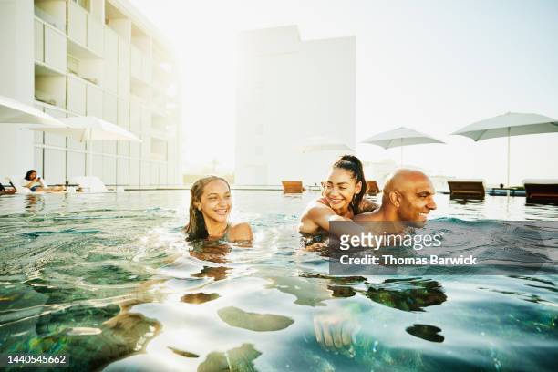 wide shot of girl relaxing in pool with parents at tropical resort - images of black families stock-fotos und bilder
