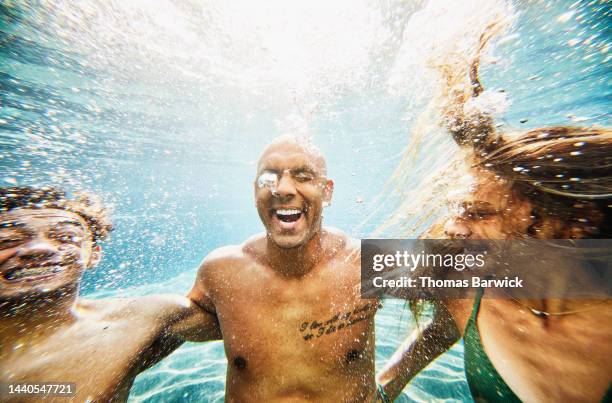 medium shot of smiling family underwater in pool at tropical resort - holiday resort family sunshine stock pictures, royalty-free photos & images