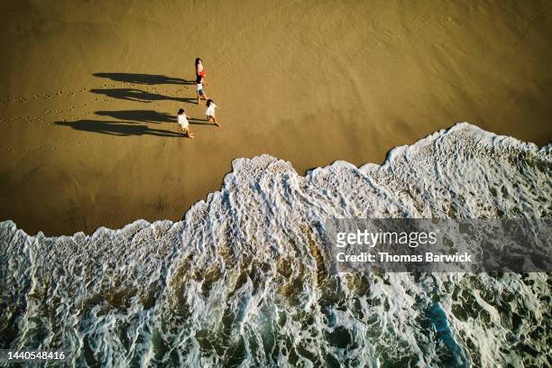 Wide aerial shot of family walking on tropical beach at sunrise