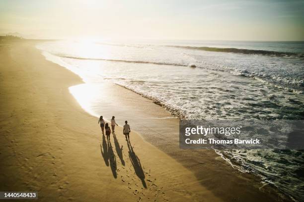 wide aerial shot of family walking on tropical beach at sunrise - asian luxury lifestyle foto e immagini stock