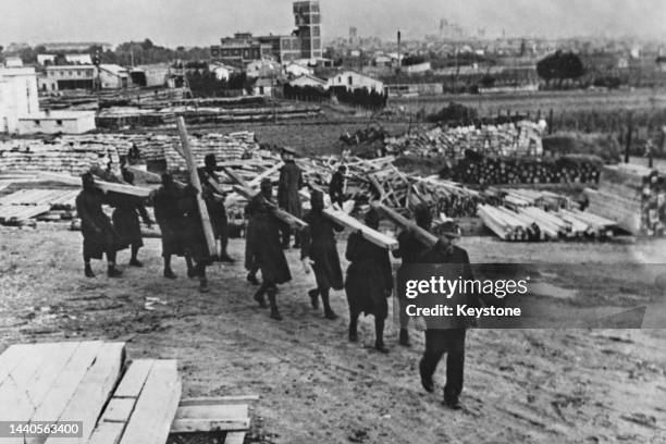 French West African colonial soldier prisoners of war working under German Wehrmacht guard carrying timber beams at a defence construction site on...