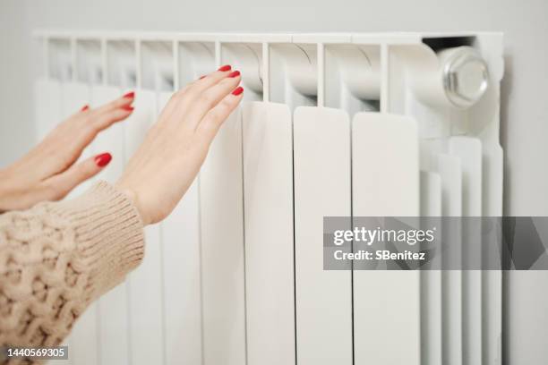 female hands touching cold ribs on home heater to check the temperature - water heater stockfoto's en -beelden