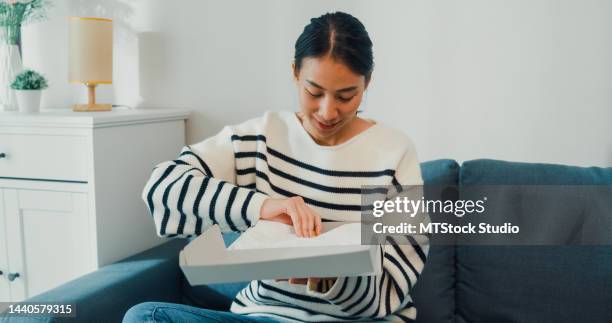 excited young happy asia girl wear sweater receiving and opening unbox white cream box gift from clothing store with happy moment on sofa couch. - t shirtvendor stock pictures, royalty-free photos & images