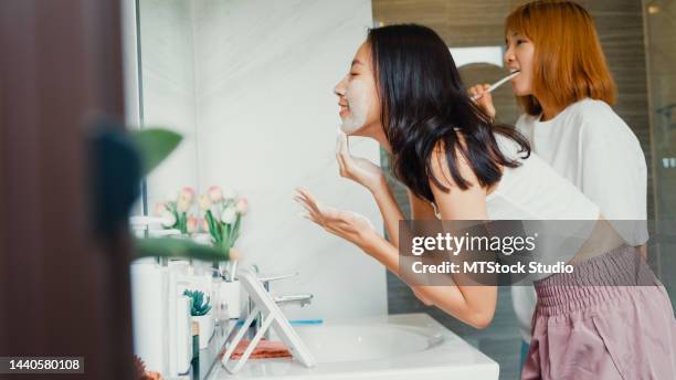 young asia lgbtq couple girls in bathroom. happy ladies have fun brush teeth and facial foam cleaning face in front of mirror together in lavatory at home. - girl in mirror stock pictures, royalty-free photos & images