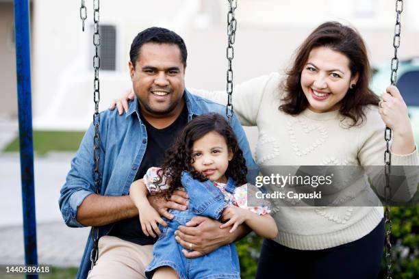 happy multiracial family on the playground swing - playground equipment happy parent stock pictures, royalty-free photos & images
