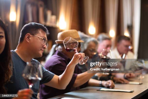 man inspecting wine in glass at crowded bar - winetasting stock pictures, royalty-free photos & images