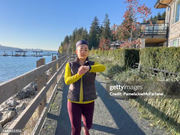 urasian young woman in exercise clothing checking smartwatch on seawalk - canadian pacific women stock pictures, royalty-free photos & images