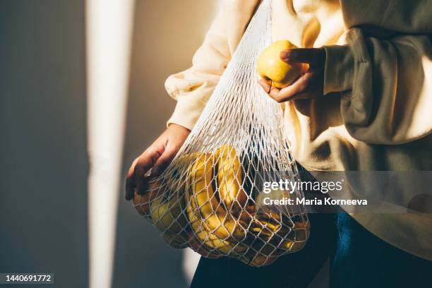 woman holding eco friendly shopping mesh bag with fruit. - shopping paper bag stock-fotos und bilder