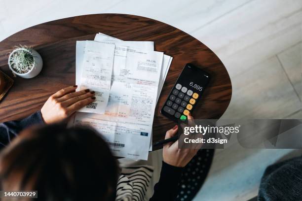 overhead view of young asian woman managing personal banking and finance at home. planning budget and calculating expenses while checking her bills with calculator. managing taxes and financial bills. home budgeting. concept of finance and economy - skuld finansväsen bildbanksfoton och bilder