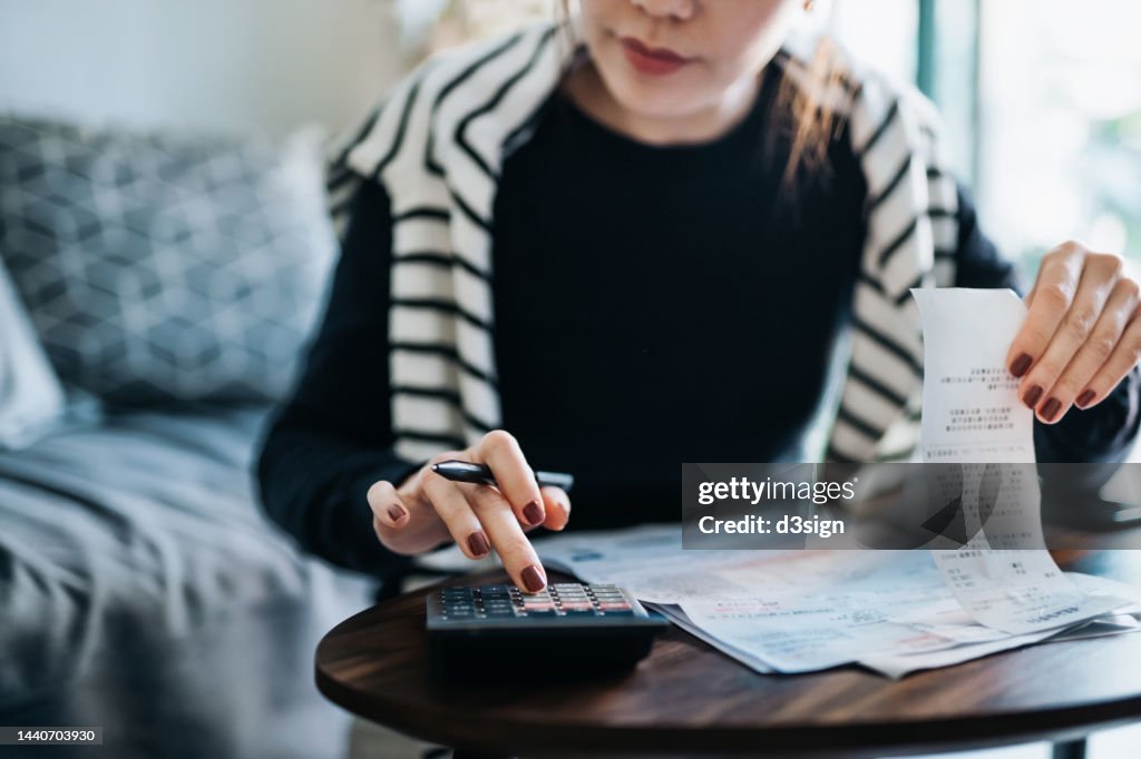 Cropped shot of young Asian woman managing personal banking and finance at home. Planning budget and calculating expenses with calculator. Managing taxes and financial bills. Wealth management. Home budgeting