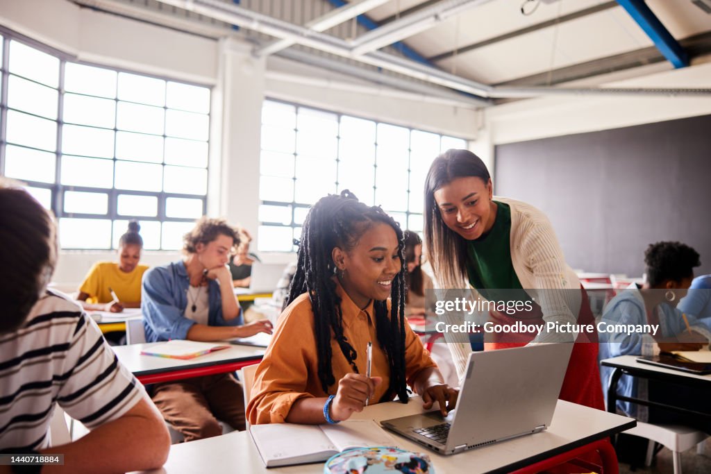 Enseignant souriant parlant avec un élève à l’aide d’un ordinateur portable pendant une leçon en classe
