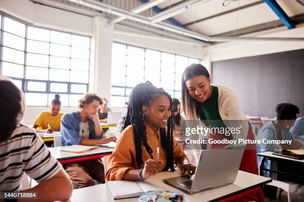 smiling teacher talking with a student using a laptop during a classroom lesson - teenagers studying imagens e fotografias de stock