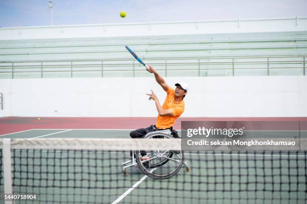 adaptive athlete practicing serve while warming up for wheelchair tennis match - wheelchair tennis stock pictures, royalty-free photos & images