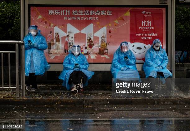 Epidemic control workers wear protective equipment as they try to stay out of the rain as they wait in front of a billboard advertising Chinas...