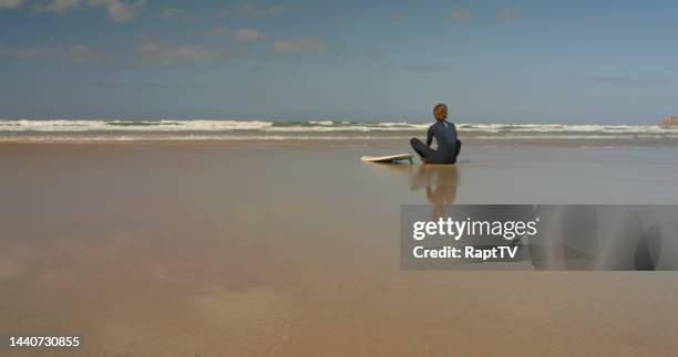 a surfer sits on a beach looking out over the breaking waves - feet run in ocean stock pictures, royalty-free photos & images