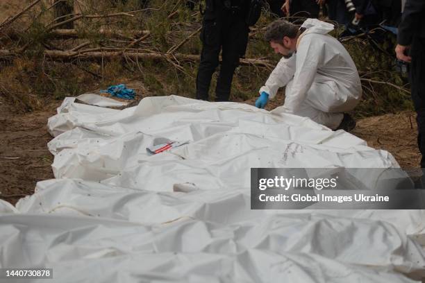 Forensic technician sat down near white body bags with exhumed bodies at the site of a mass burial in a forest during exhumation on September 16,...