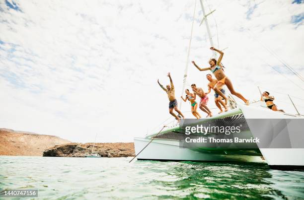 Wide shot of families jumping into ocean from deck of sailboat
