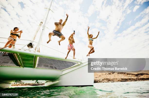 wide shot of mother filming family jumping into ocean from sailboat - father son sailing stock pictures, royalty-free photos & images