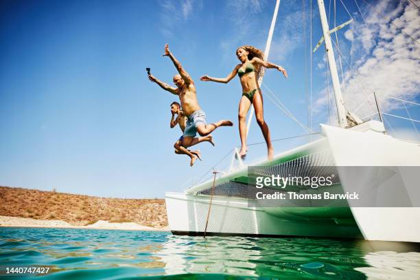 wide shot of family jumping into tropical ocean from deck of sailboat - preteen girl no shirt stock pictures, royalty-free photos & images