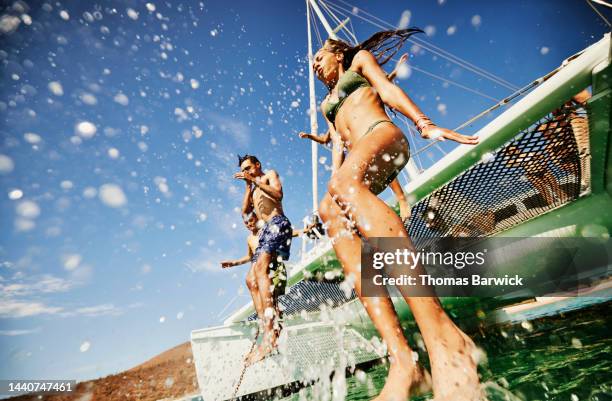 wide shot of friends jumping into tropical ocean from deck of sailboat - girl takes shirt off foto e immagini stock