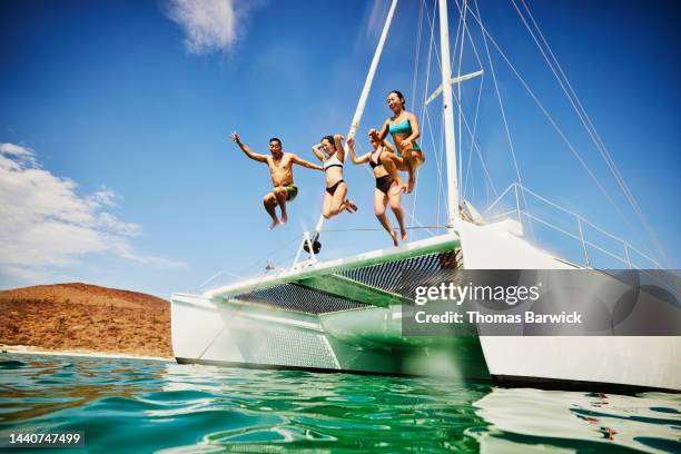 wide shot of family jumping into tropical ocean from deck of sailboat - jumping of boat photos et images de collection