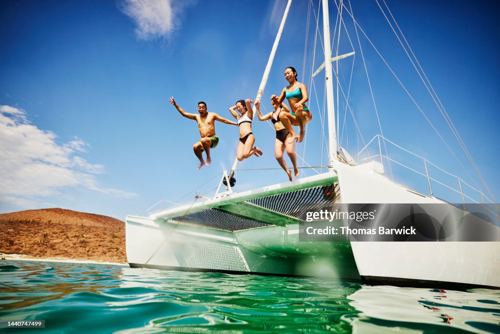 Wide shot of family jumping into tropical ocean from deck of sailboat