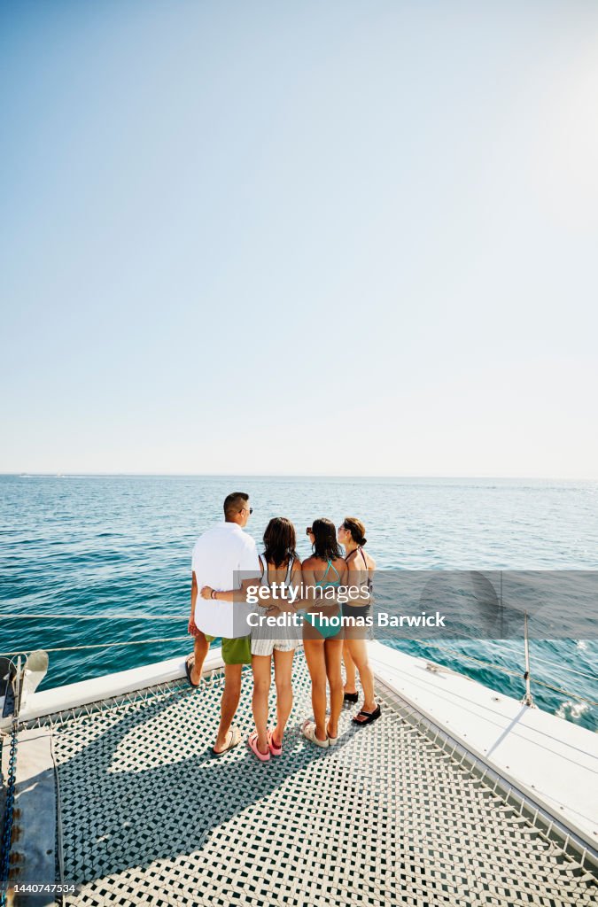 Wide shot rear view of embracing family standing at bow of catamaran