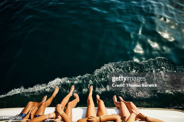 medium shot of teenagers feet hanging over side of sailboat - kreuzfahrt stock-fotos und bilder