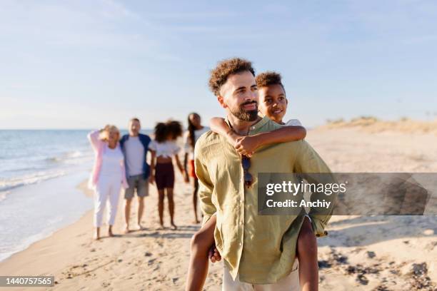 glücklicher vater, der seinem kleinen jungen eine huckepackfahrt am strand gibt - extended family outdoors spring stock-fotos und bilder